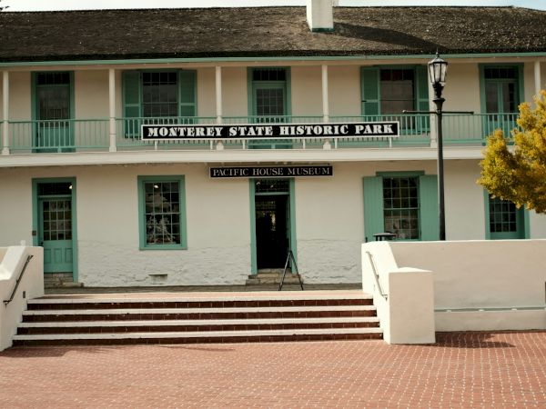 A two-story white building with green railings and a sign reading &ldquo;Granary School History Club,&rdquo; red brick steps, and a wide brick plaza in front.