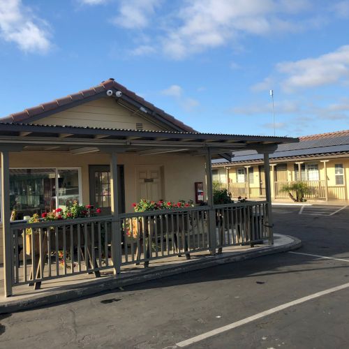 Courtyard of a school building with awning, railings, flower planters, and solar panels under a bright blue sky.