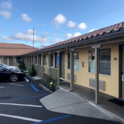 Single-story building with tiled roof, parking spots, a black car, and a wheelchair-accessible sign under a blue sky.