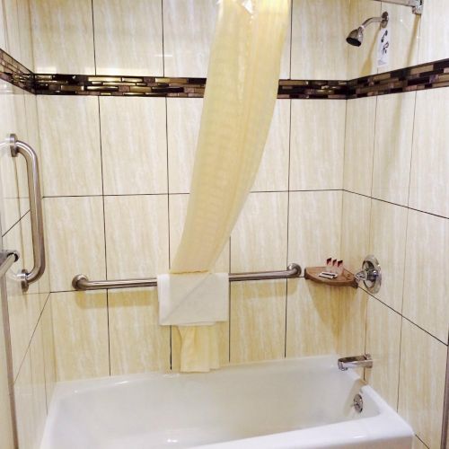 A hotel bathroom shower with tiled walls, a sliding glass door, grab bars, and towels hanging.