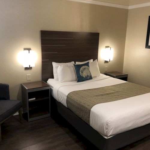 A modern hotel bedroom with a made bed, side tables, lit wall lamps, and framed marine art on the walls.