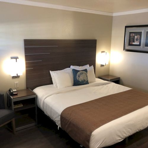 A hotel-style bedroom with a made bed, nightstands, wall lamps, and framed art on the walls.