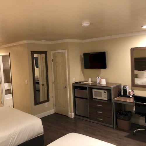 A hotel room setup with two beds, a desk, TV, microwave/coffee maker, and a large wall mirror.