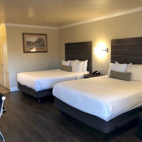 A hotel room with two neatly made queen beds, dark headboards, pillows, bedside lamps, and framed wall art.