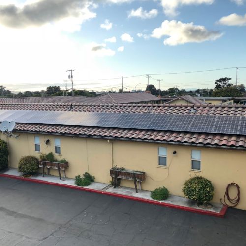 Rooftop of a house with solar panels installed, under a bright partly cloudy sky.