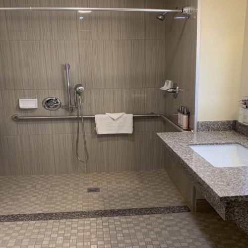 A modern hotel bathroom with a walk-in shower, granite sink, and tiled floor, plus towels and toiletries.