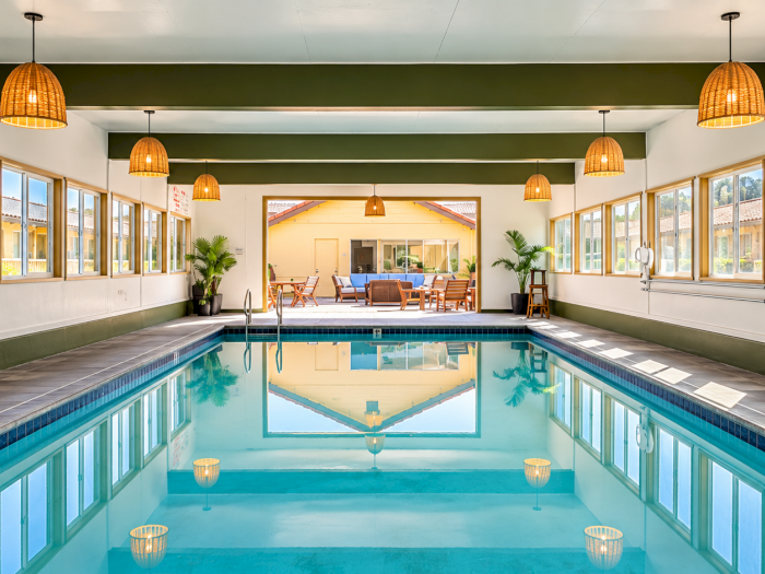 Indoor swimming pool with windows, sunlit lounge chairs, and warm hanging lantern lights above.